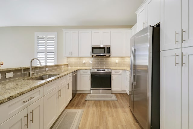 kitchen with appliances with stainless steel finishes, white cabinetry, light stone countertops, light hardwood / wood-style floors, and sink