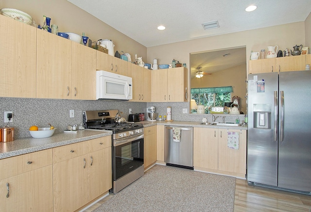 kitchen with light brown cabinets, appliances with stainless steel finishes, and light hardwood / wood-style flooring