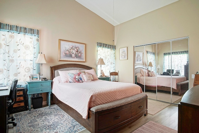 bedroom with light wood-type flooring, high vaulted ceiling, and a closet