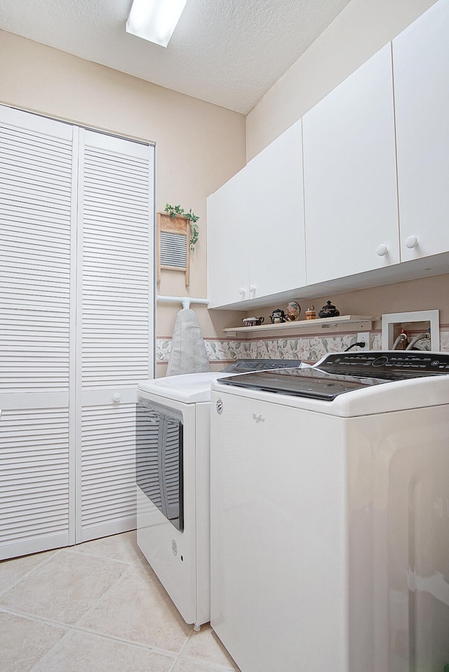 laundry area featuring a textured ceiling, separate washer and dryer, light tile patterned floors, and cabinets