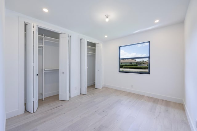 unfurnished bedroom featuring multiple closets and light hardwood / wood-style flooring