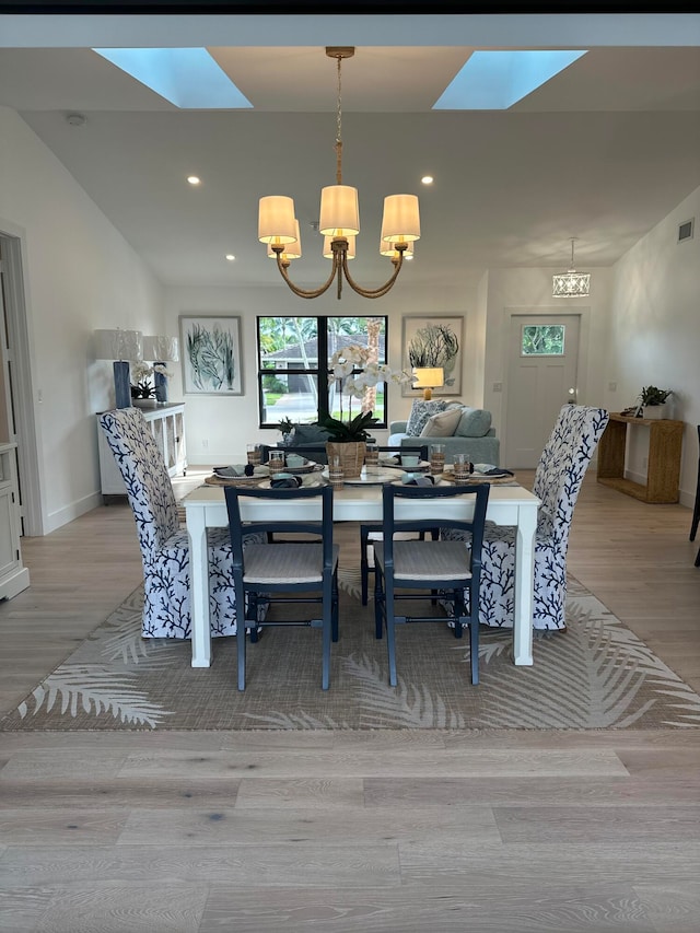 dining space with a skylight, a notable chandelier, and light hardwood / wood-style flooring