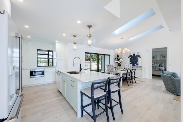 kitchen with sink, a kitchen island with sink, white cabinetry, light wood-type flooring, and white appliances