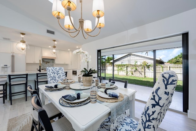 dining room with light hardwood / wood-style floors, a notable chandelier, and vaulted ceiling