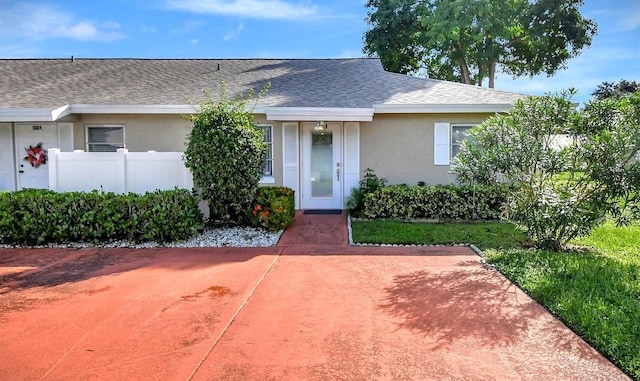 view of front facade with a shingled roof, fence, and stucco siding