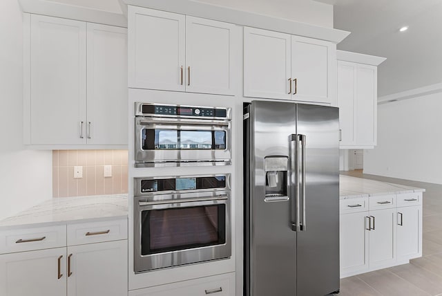 kitchen featuring tasteful backsplash, light stone countertops, appliances with stainless steel finishes, and white cabinets