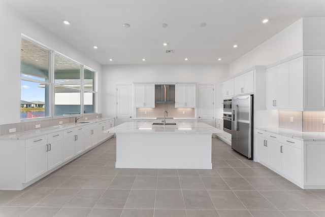 kitchen with sink, white cabinetry, backsplash, high quality fridge, and a center island with sink