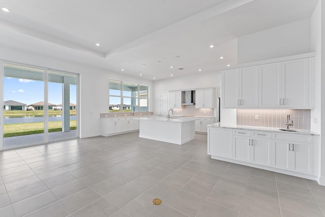 kitchen with white cabinetry, a kitchen island with sink, a water view, tasteful backsplash, and light tile patterned flooring