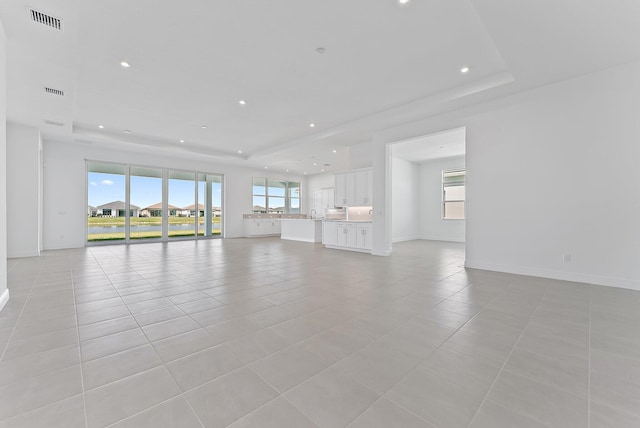 unfurnished living room featuring plenty of natural light, a raised ceiling, and light tile patterned floors