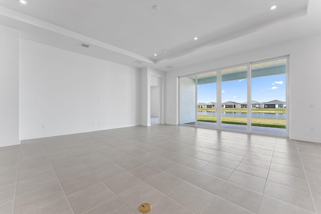 tiled spare room with a water view and a raised ceiling