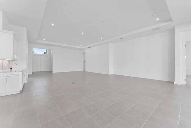 unfurnished living room featuring a raised ceiling, sink, and light tile patterned floors