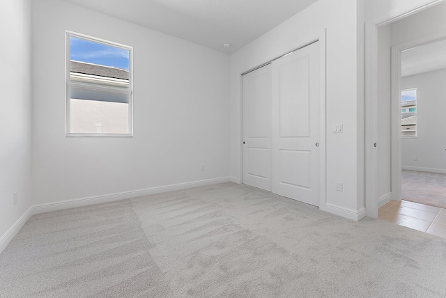 unfurnished bedroom featuring multiple windows, light carpet, and a closet