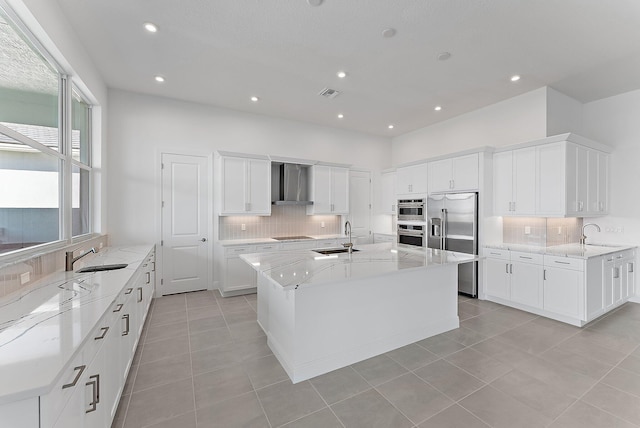 kitchen with wall chimney range hood, sink, an island with sink, and built in refrigerator