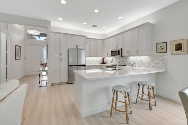 kitchen featuring backsplash, appliances with stainless steel finishes, a breakfast bar area, light wood-type flooring, and sink