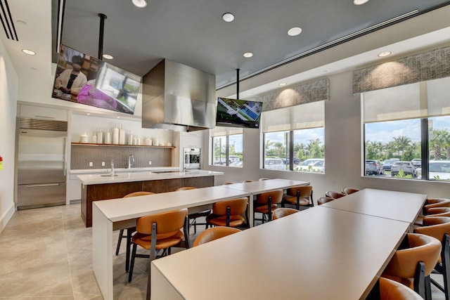 kitchen featuring plenty of natural light, wall chimney exhaust hood, appliances with stainless steel finishes, and an island with sink