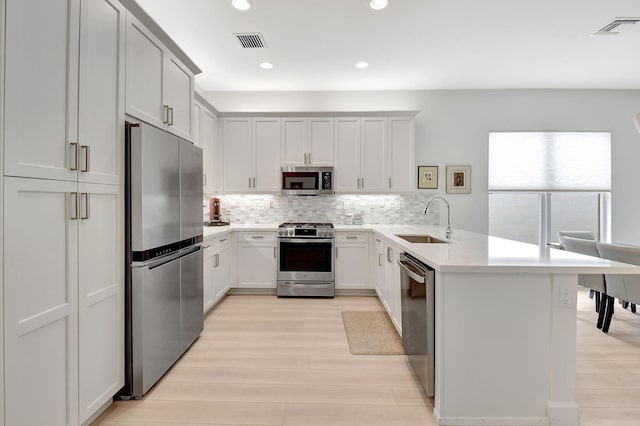 kitchen with kitchen peninsula, tasteful backsplash, appliances with stainless steel finishes, light hardwood / wood-style flooring, and sink