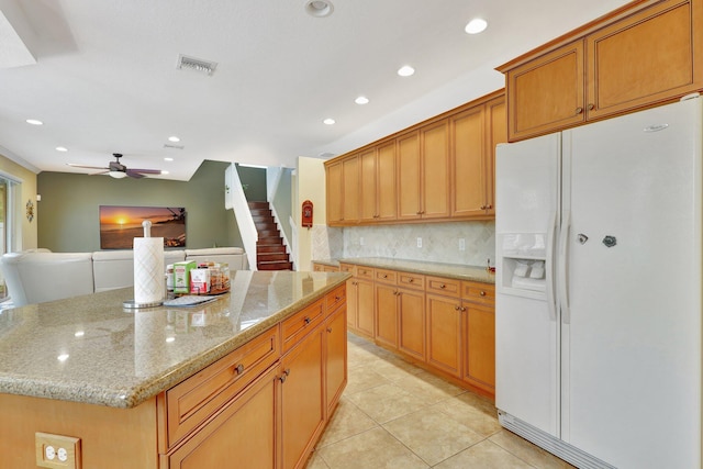 kitchen featuring light stone counters, ceiling fan, light tile patterned flooring, a kitchen island, and white refrigerator with ice dispenser