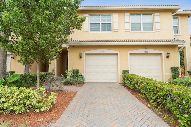 view of property with stucco siding, a tiled roof, decorative driveway, and a garage