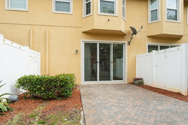 entrance to property featuring a patio area, stucco siding, and fence