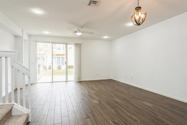 spare room with visible vents, ceiling fan with notable chandelier, dark wood-style floors, baseboards, and stairs