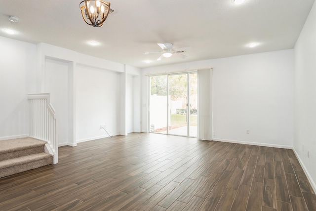 empty room featuring stairway, ceiling fan with notable chandelier, baseboards, and dark wood-style flooring