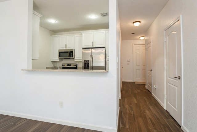 kitchen with white cabinets, appliances with stainless steel finishes, dark hardwood / wood-style flooring, and light stone counters