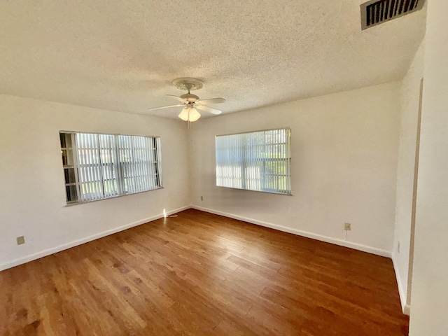 spare room with visible vents, ceiling fan, a textured ceiling, wood finished floors, and baseboards