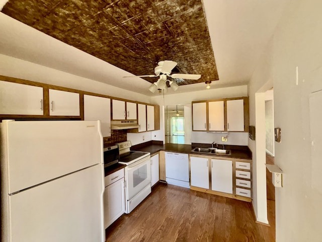 kitchen with under cabinet range hood, white appliances, a sink, dark countertops, and an ornate ceiling