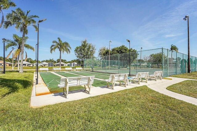 view of community featuring shuffleboard, a yard, fence, and a tennis court