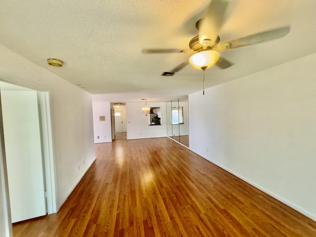 unfurnished living room featuring ceiling fan with notable chandelier, visible vents, a textured ceiling, and wood finished floors