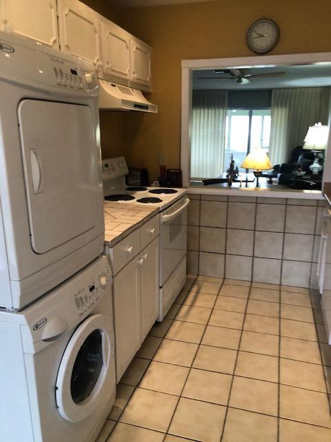 kitchen with tile countertops, stacked washer and clothes dryer, electric range, light tile patterned flooring, and white cabinetry