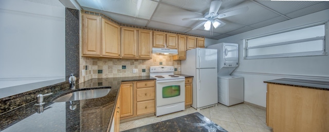 kitchen with light tile patterned flooring, white appliances, a paneled ceiling, dark stone countertops, and stacked washer and dryer