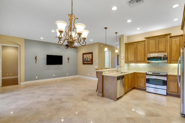 kitchen featuring light stone counters, hanging light fixtures, sink, kitchen peninsula, and stainless steel appliances