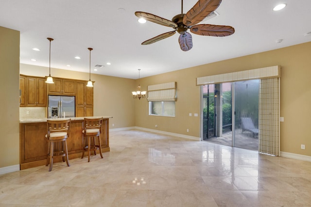 kitchen featuring stainless steel fridge, pendant lighting, tasteful backsplash, ceiling fan with notable chandelier, and a breakfast bar