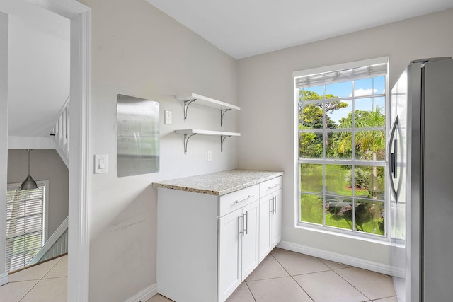 interior space featuring light stone countertops, stainless steel fridge, white cabinets, and light tile patterned flooring