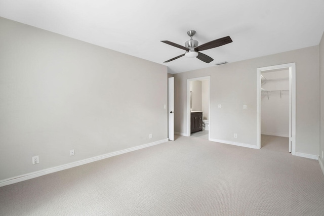 unfurnished bedroom featuring light carpet, ceiling fan, a spacious closet, connected bathroom, and a closet