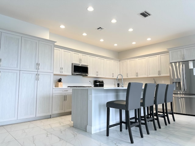 kitchen featuring a kitchen breakfast bar, an island with sink, gray cabinetry, stainless steel appliances, and sink