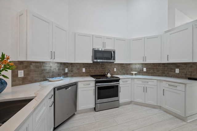 4561 Carlton Golf Dr, Lake Worth, FL 33449 - kitchen featuring light stone counters, stainless steel appliances, light wood-style flooring, white cabinets, and backsplash