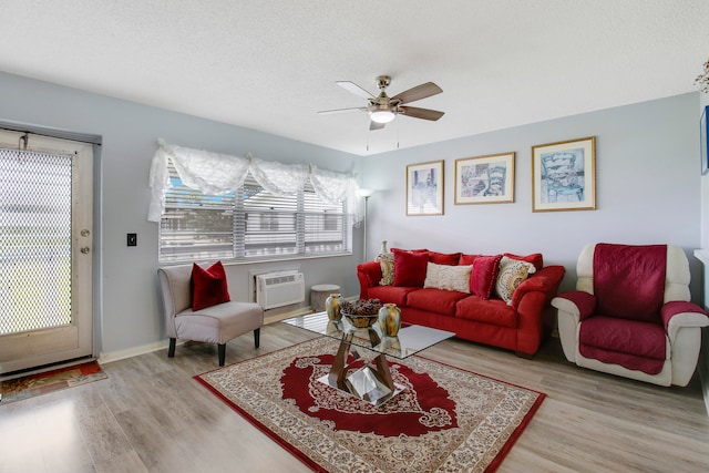 living room with an AC wall unit, light wood-type flooring, ceiling fan, and a textured ceiling