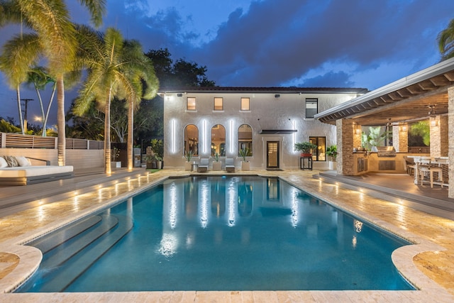 pool at dusk featuring a patio area and exterior kitchen