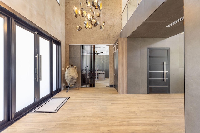 corridor with a notable chandelier, light hardwood / wood-style floors, a high ceiling, and french doors