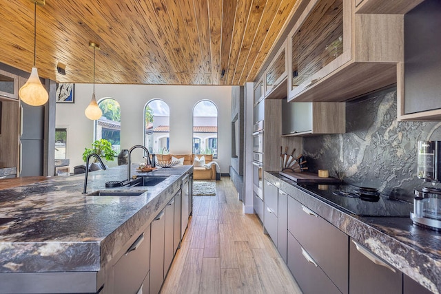 kitchen with hanging light fixtures, light hardwood / wood-style flooring, dark stone countertops, black electric cooktop, and decorative backsplash