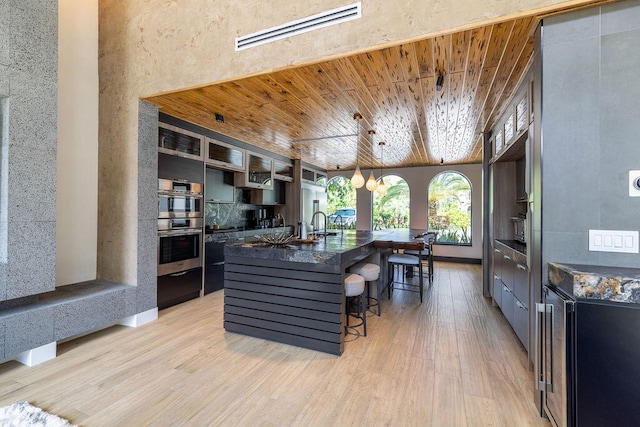 kitchen with a center island with sink, a kitchen breakfast bar, wooden ceiling, and light hardwood / wood-style flooring