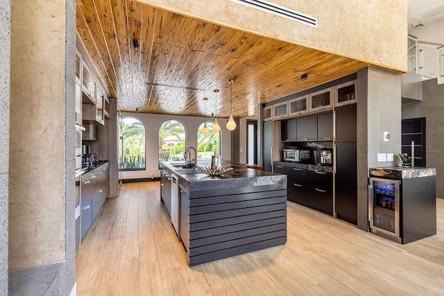 kitchen featuring sink, beverage cooler, a center island with sink, wood ceiling, and light wood-type flooring