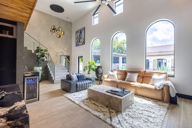 living room with wine cooler, a towering ceiling, light hardwood / wood-style flooring, and ceiling fan