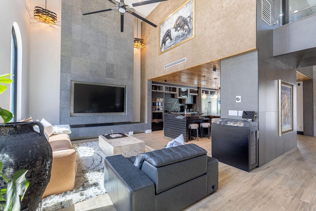 living room featuring ceiling fan, a towering ceiling, and light hardwood / wood-style floors