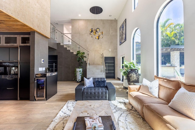 living room featuring light hardwood / wood-style floors, beverage cooler, a towering ceiling, and a wealth of natural light