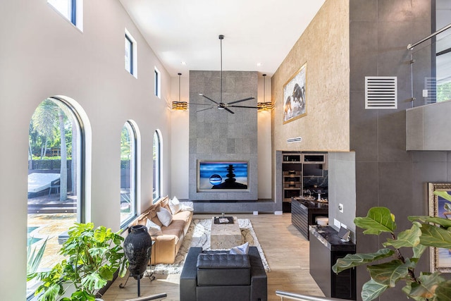 living room featuring ceiling fan, a towering ceiling, and light wood-type flooring