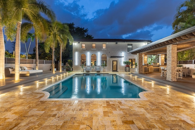 pool at dusk with an outdoor kitchen and a patio