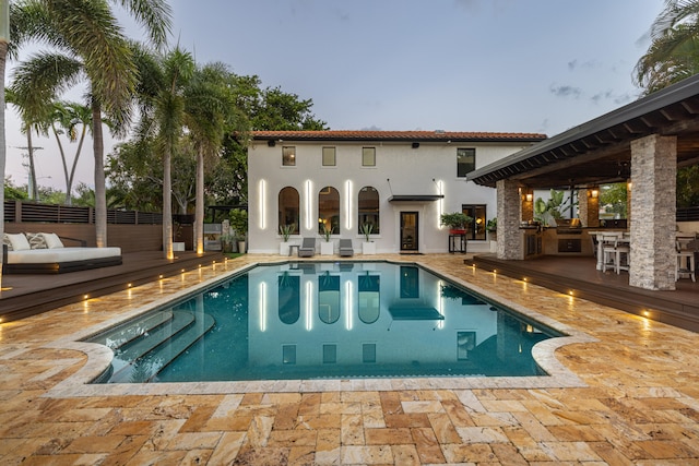 pool at dusk with a bar, a patio area, and a deck